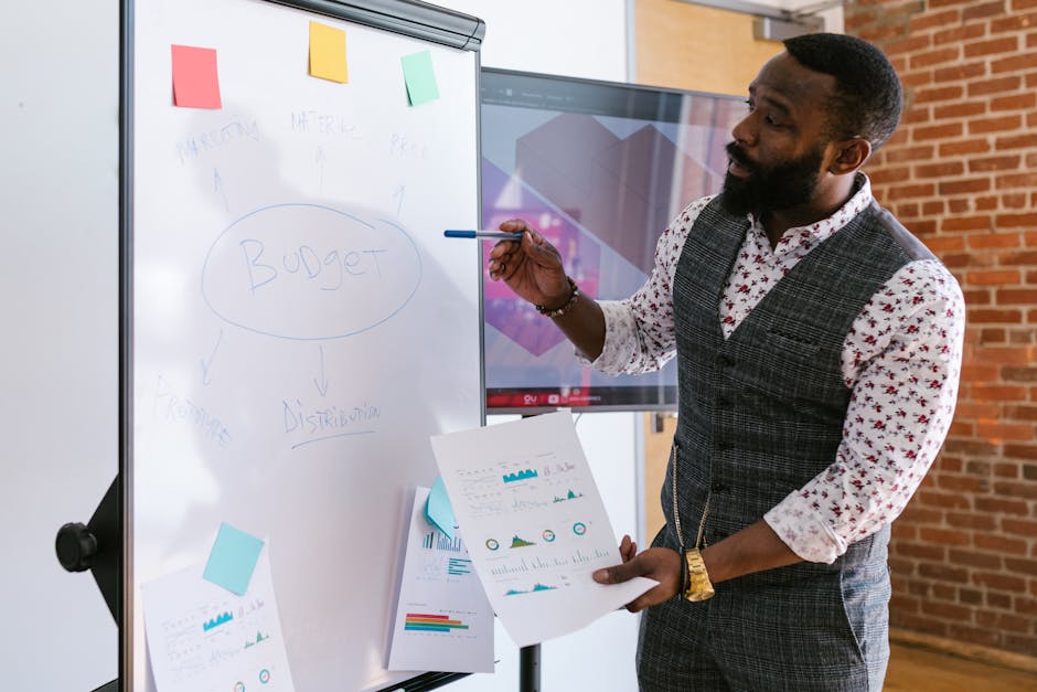 A businessman explains budget strategies using a whiteboard in an office setting.